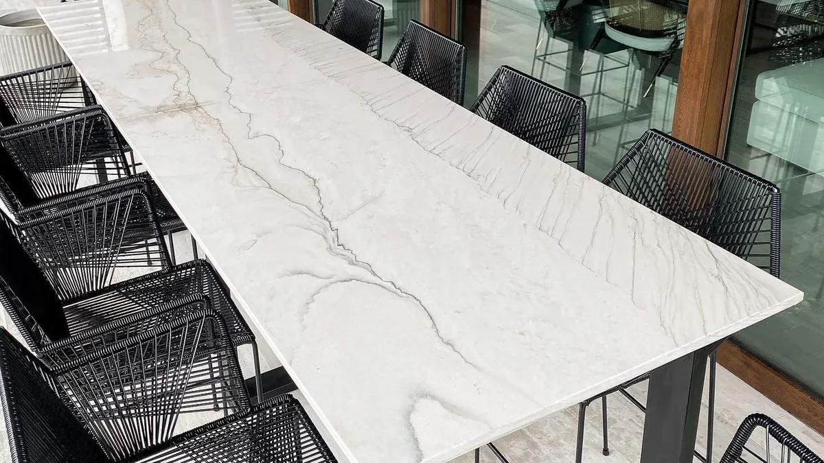 Mesa de comedor larga con cubierta de piedra natural clara y sillas negras, fabricada por Tempus