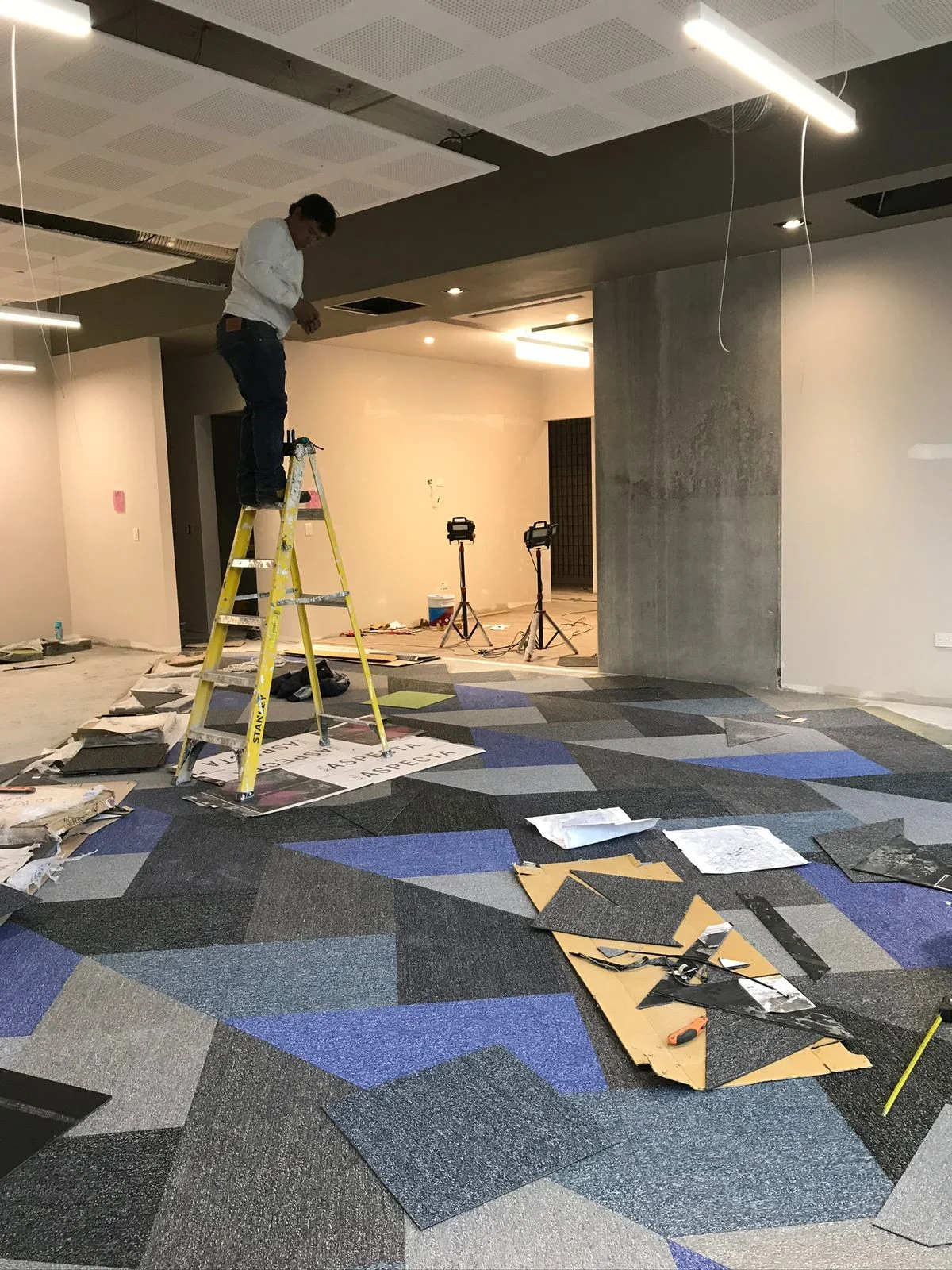 Trabajador instalando luminaria sobre alfombra modular azul, verde y gris — Altos del Roble Tempus