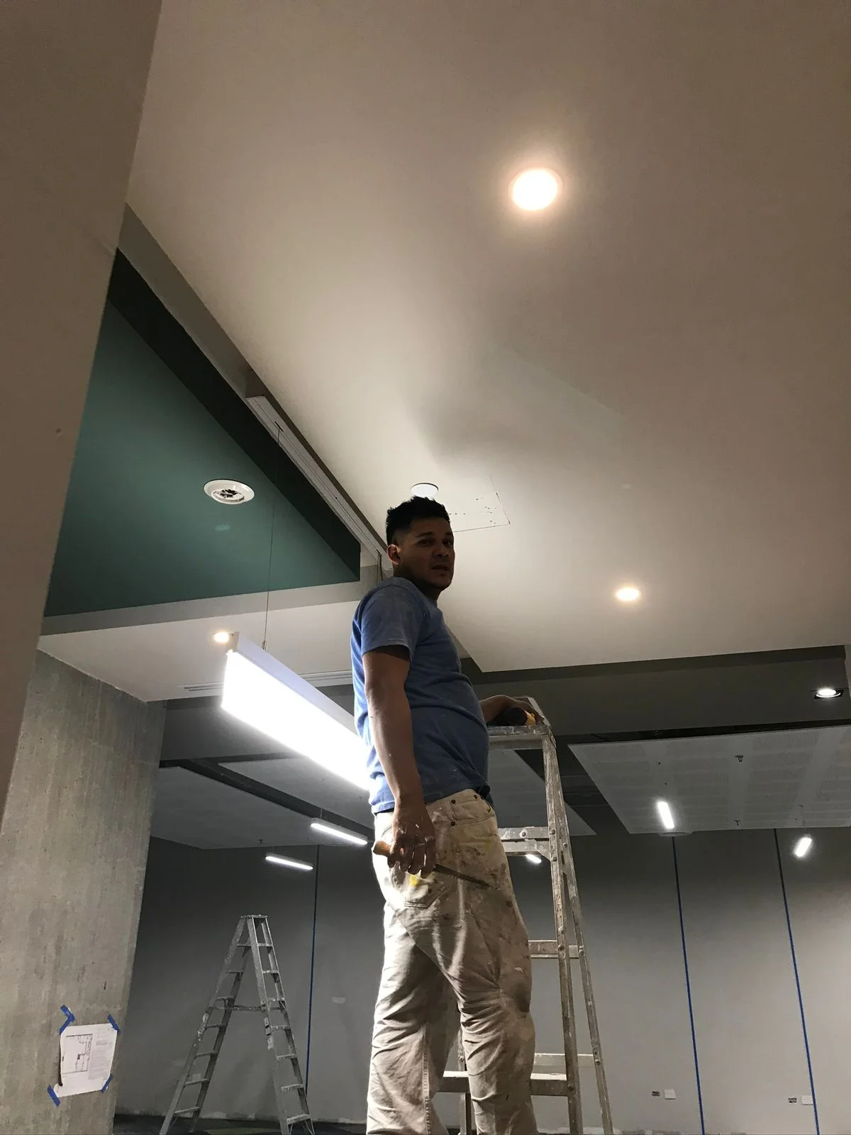 Trabajador en escalera terminando muros con plafón con downlights encendidos — Altos del Roble Tempus