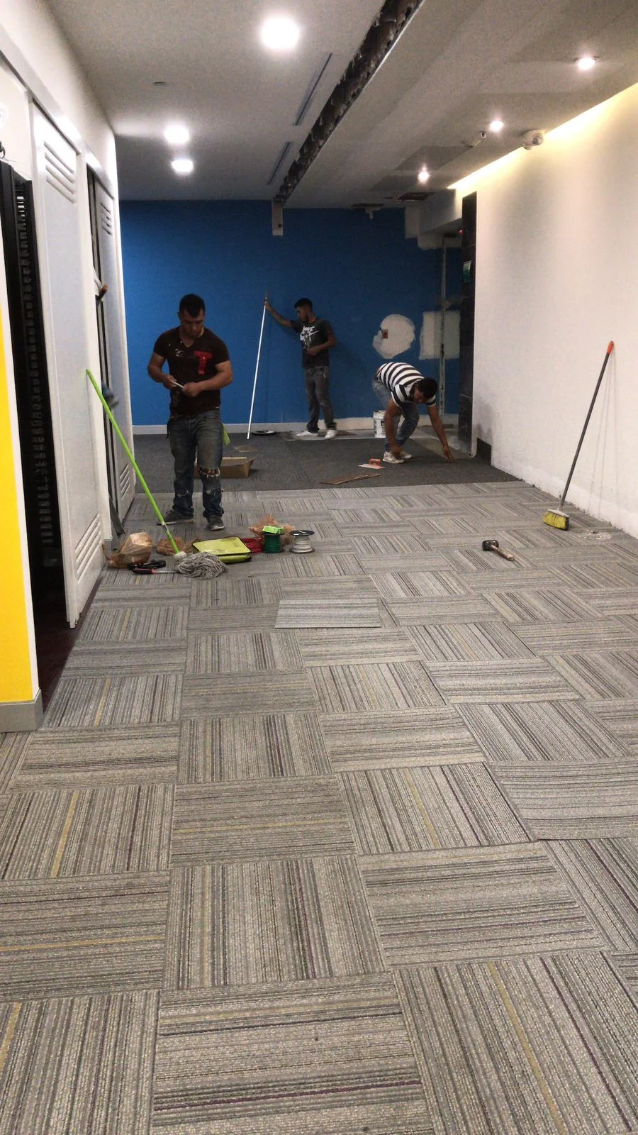 Pasillo con pared acentuada azul y trabajadores limpiando alfombra modular — Altos del Roble Tempus