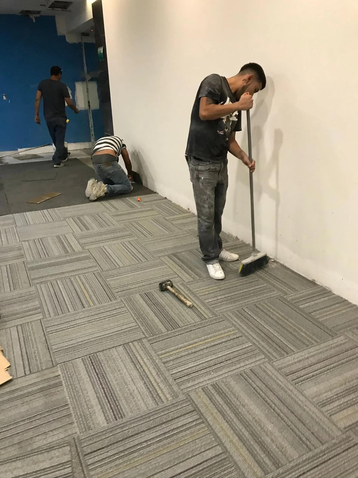 Trabajadores barriendo alfombra modular y resanando muro azul al fondo — Altos del Roble Tempus Monterrey