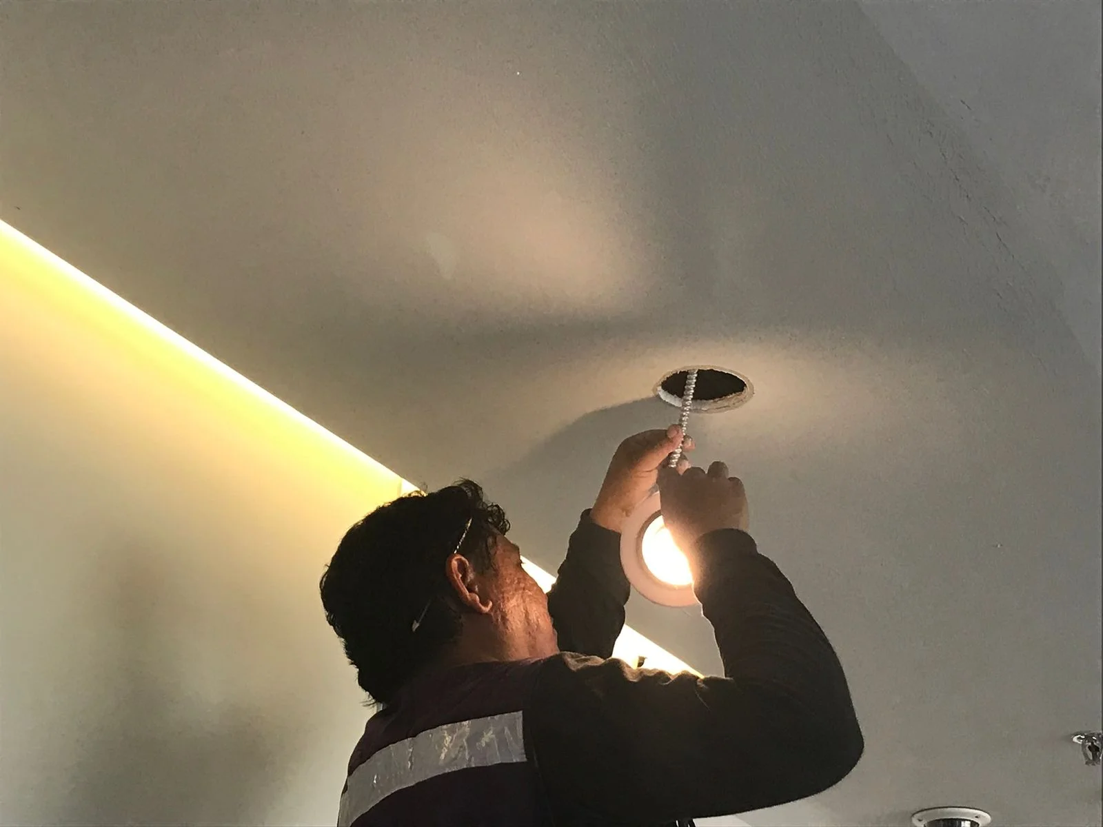 Trabajador instalando luminaria empotrada con cove de luz indirecta cálida — Altos del Roble Tempus
