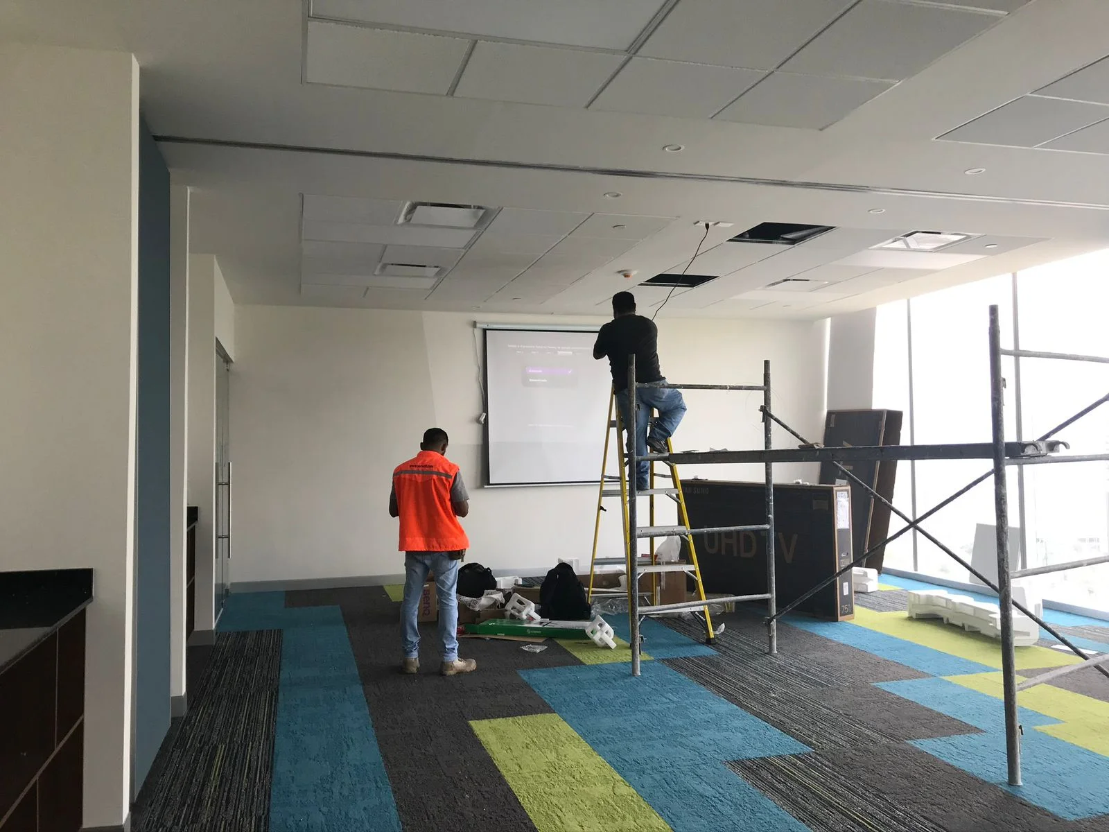 Sala de capacitación con pizarra, trabajadores en escalera y alfombra geométrica — Altos del Roble Tempus