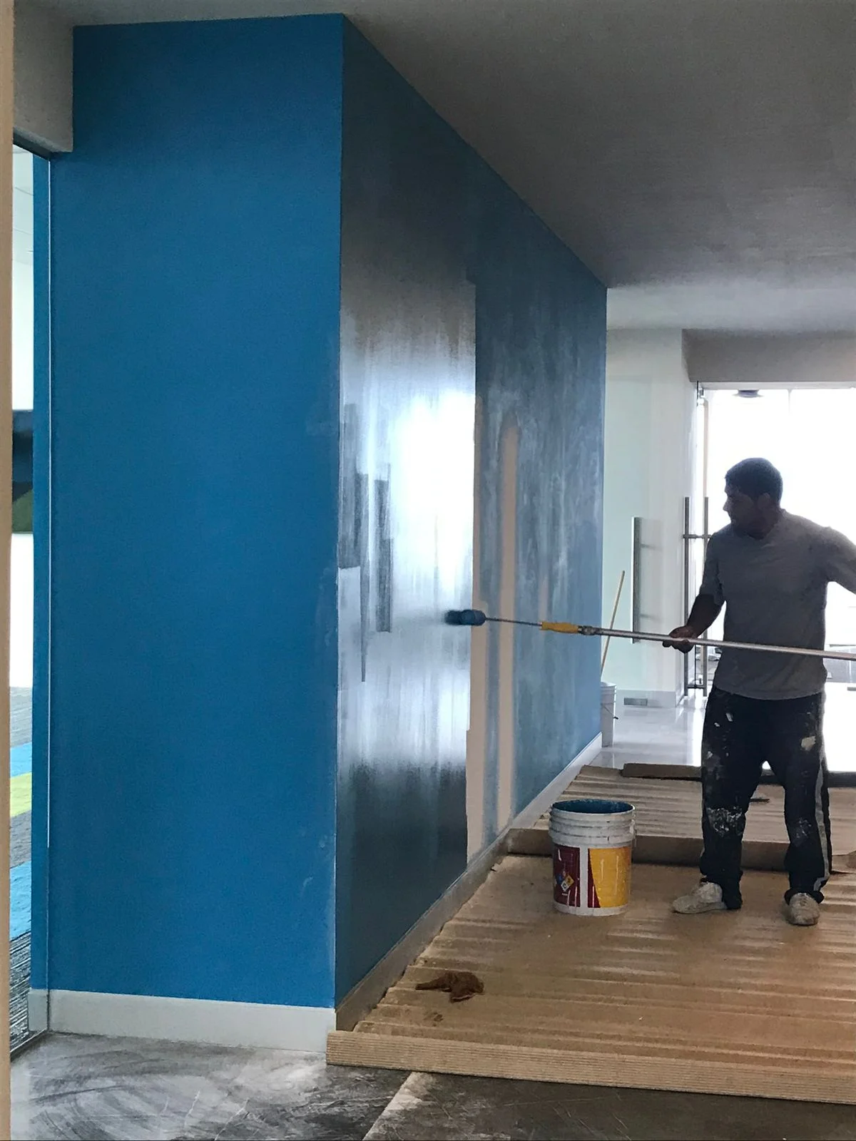 Trabajador aplicando pintura azul brillante con extensión de rodillo en muro alto — Altos del Roble Tempus