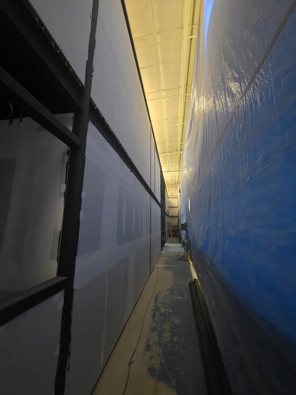 Pasillo angosto entre muros altos de tablaroca con plástico protector azul — Grupo Hydro Tempus