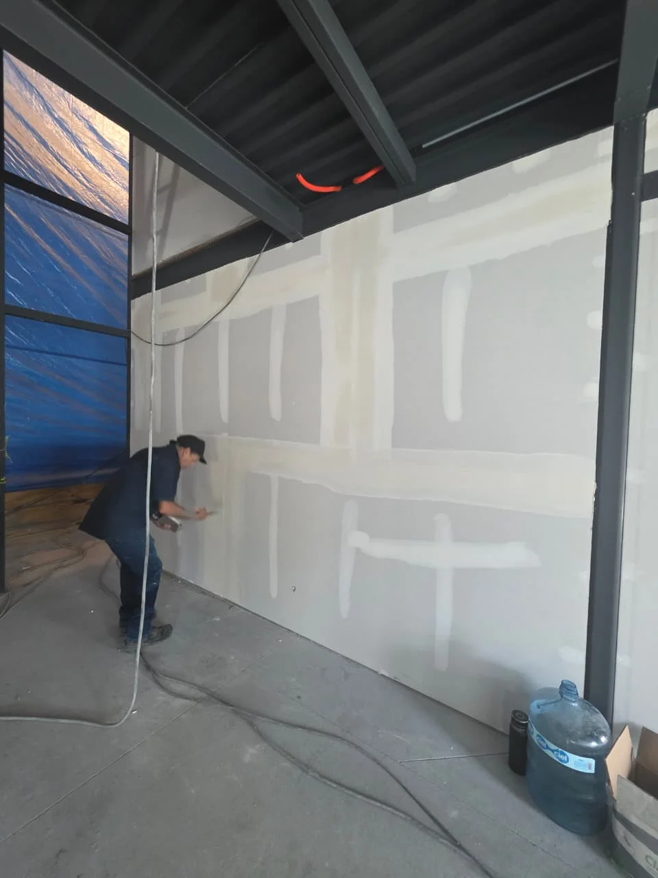 Trabajador resanando juntas en muro alto de tablaroca con cortina protectora azul — Grupo Hydro Tempus