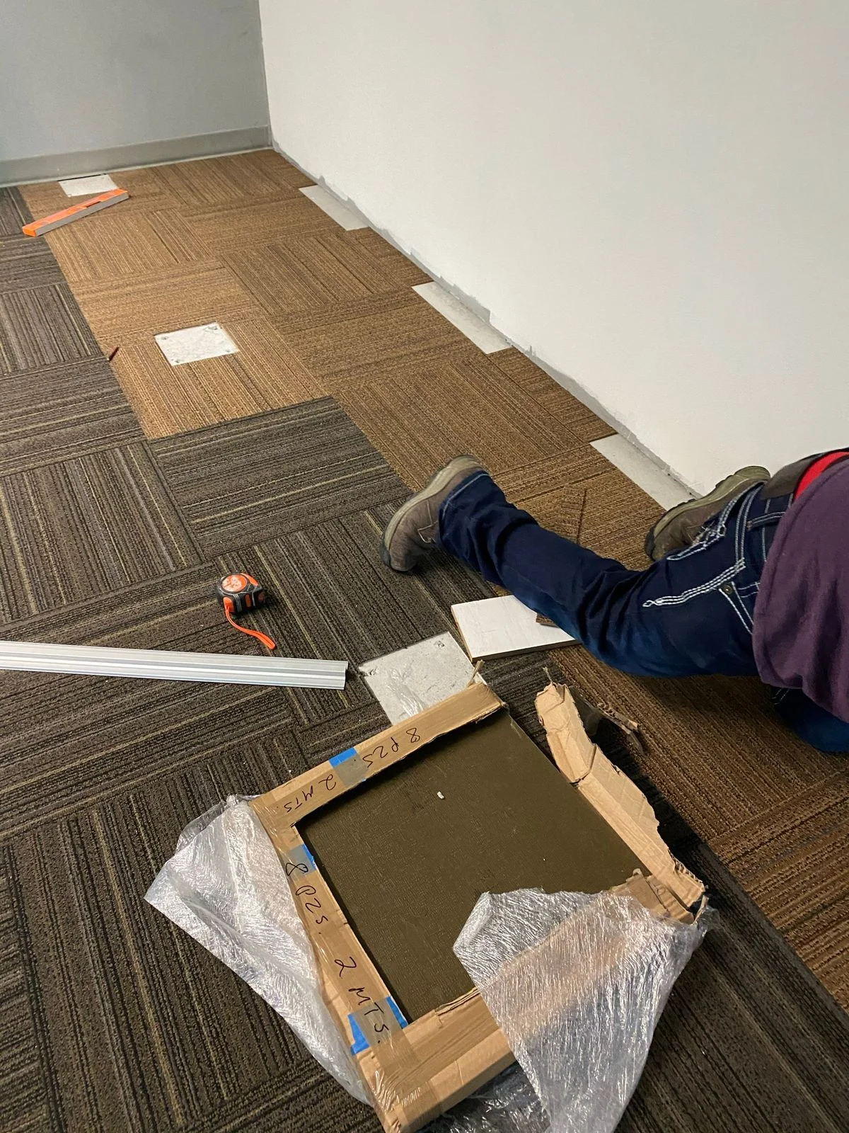 Detalle de instalación de alfombra modular sobre piso de concreto con cinta métrica — Nórdika Business Center Tempus