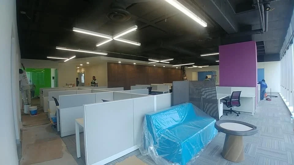 Open office con plafón industrial negro, luminarias lineales en patrón cruzado y paneles magenta — Nórdika Business Center Tempus